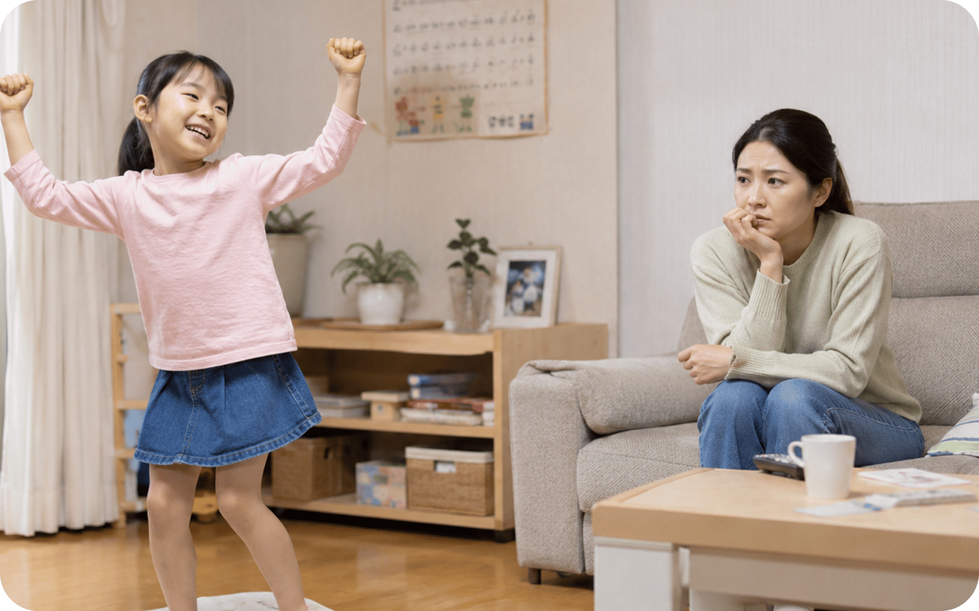 거실에서 아이가 두 팔을 들고 즐거워하는 옆에서 근심스러운 표정으로 지켜보는 보호자